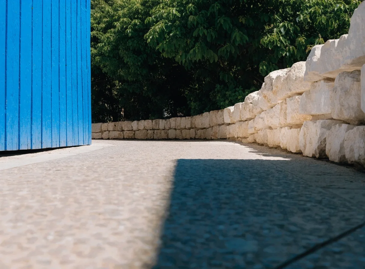 Cobalt-blue garden wall meeting pale stone at noon, seen from a low path edge