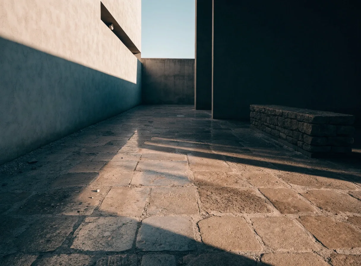 Quiet courtyard with cool shadowed wall, hard-lit floor, and an empty bench