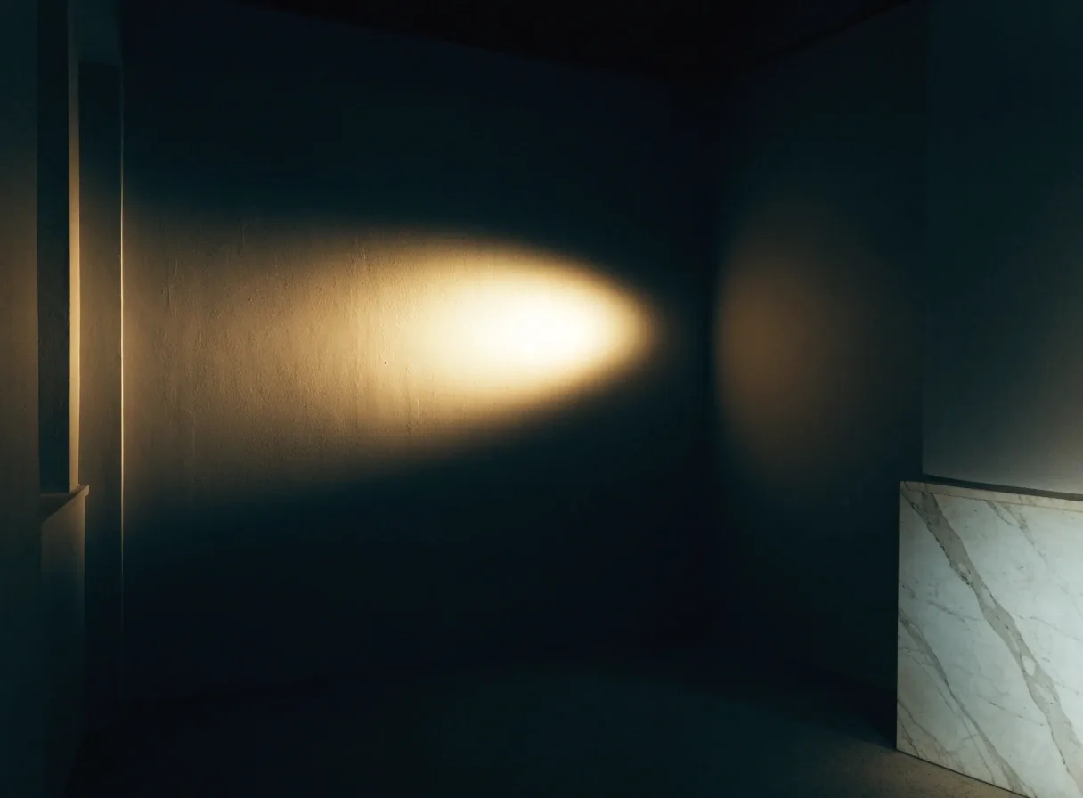 Dim museum interior with a hard pool of light on the back wall and a lit marble corner in the lower right