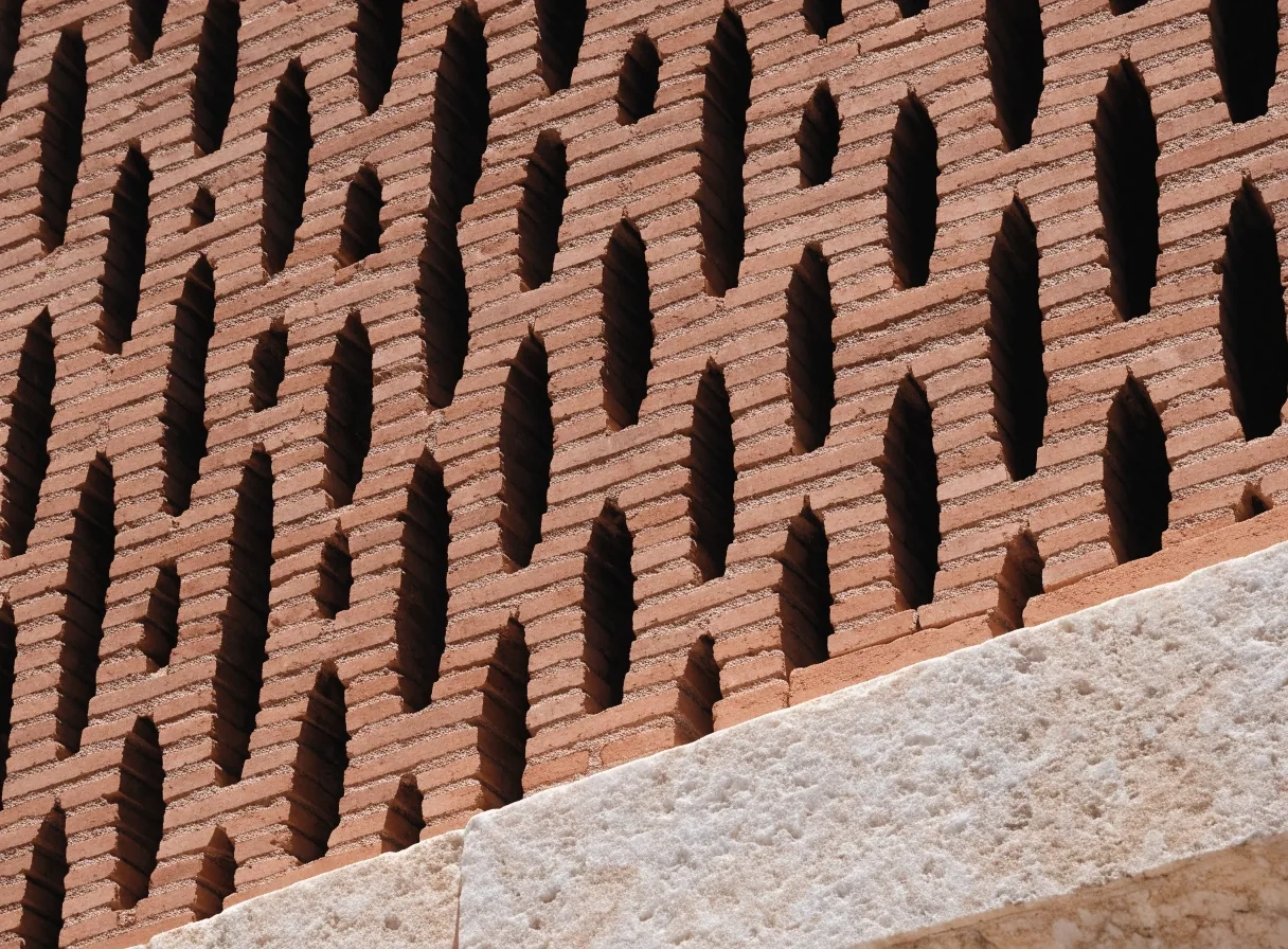 Macro detail of the terracotta brick lattice screen catching hard noon light, with a coursed marble block entering the lower frame