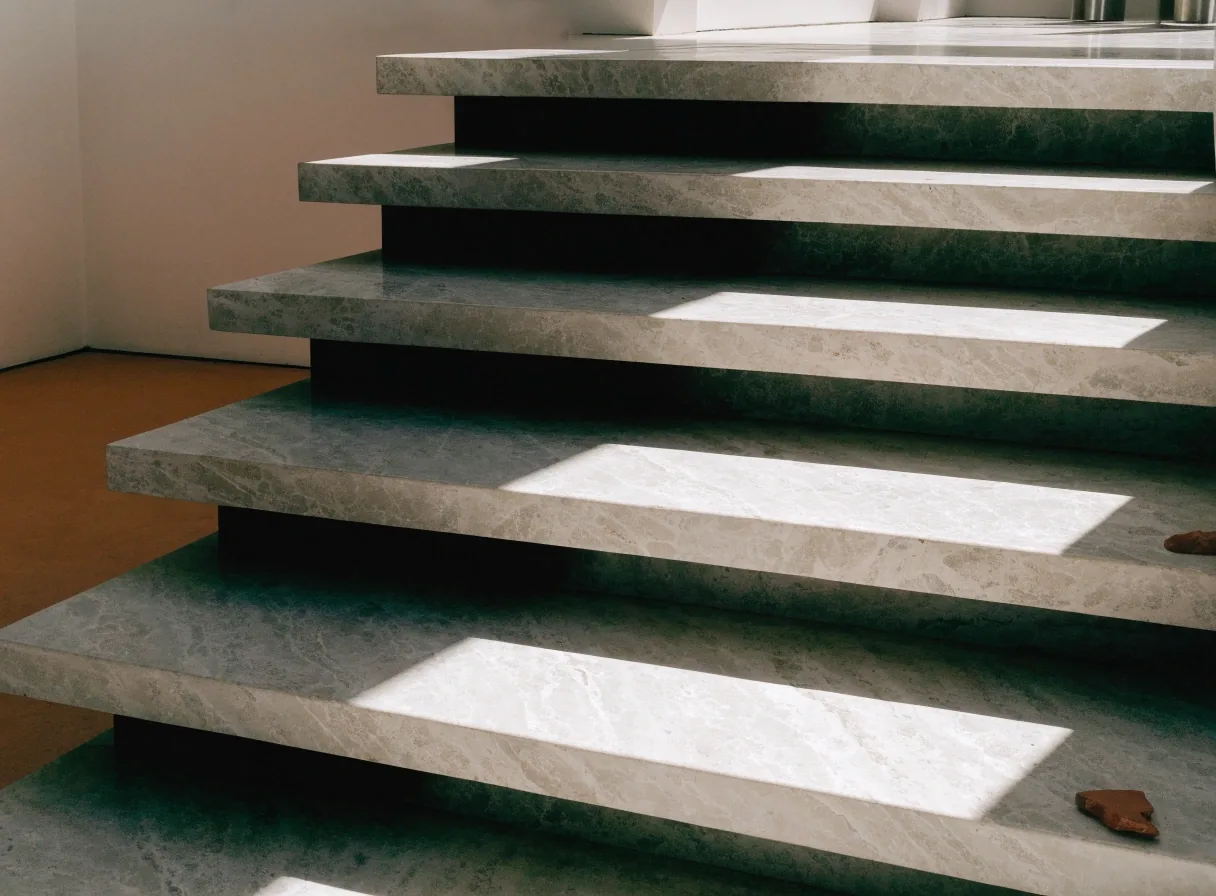 Pale marble stair treads with a hard diagonal noon shadow falling across them and a terracotta floor edge at the lower left