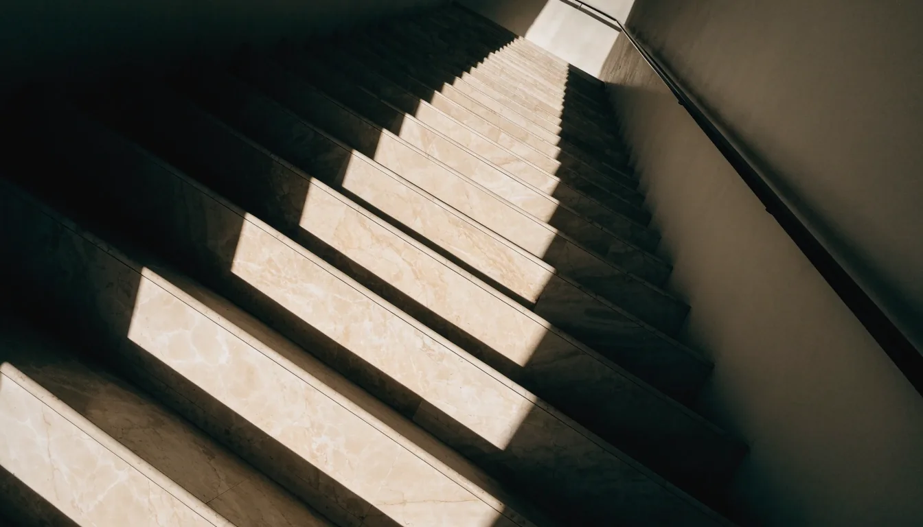Marble stair treads seen from below, deep self-shadow under each step and a rail shadow crossing the wall