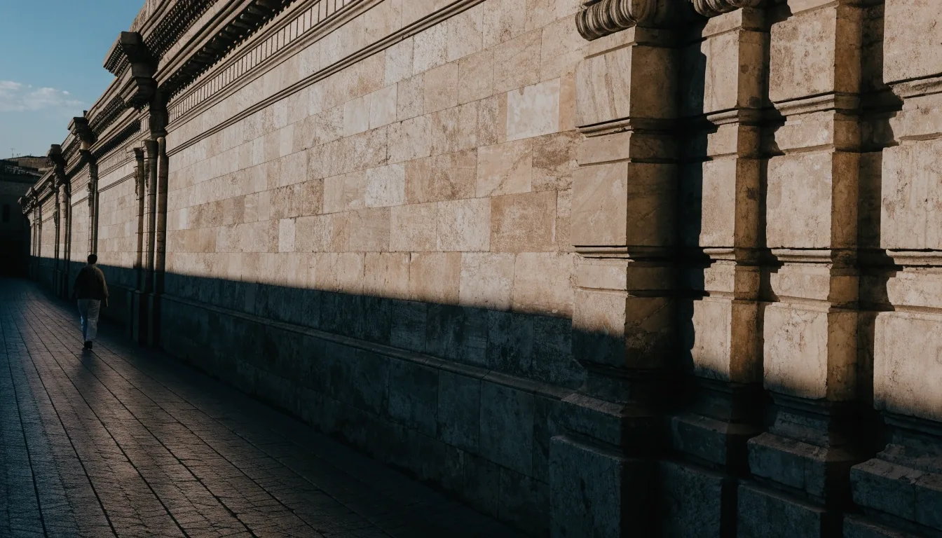 Museum exterior wall running along a paved walkway in hard directional light